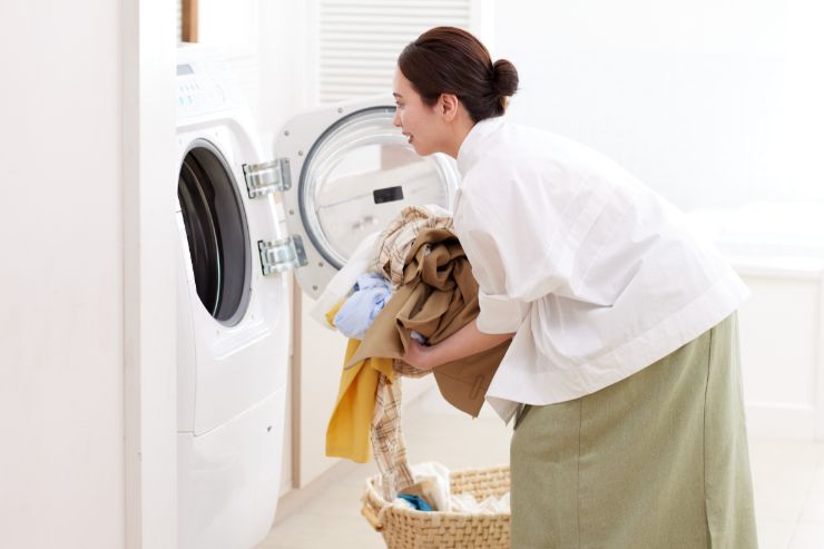 donna con bucato in mano accanto la lavatrice